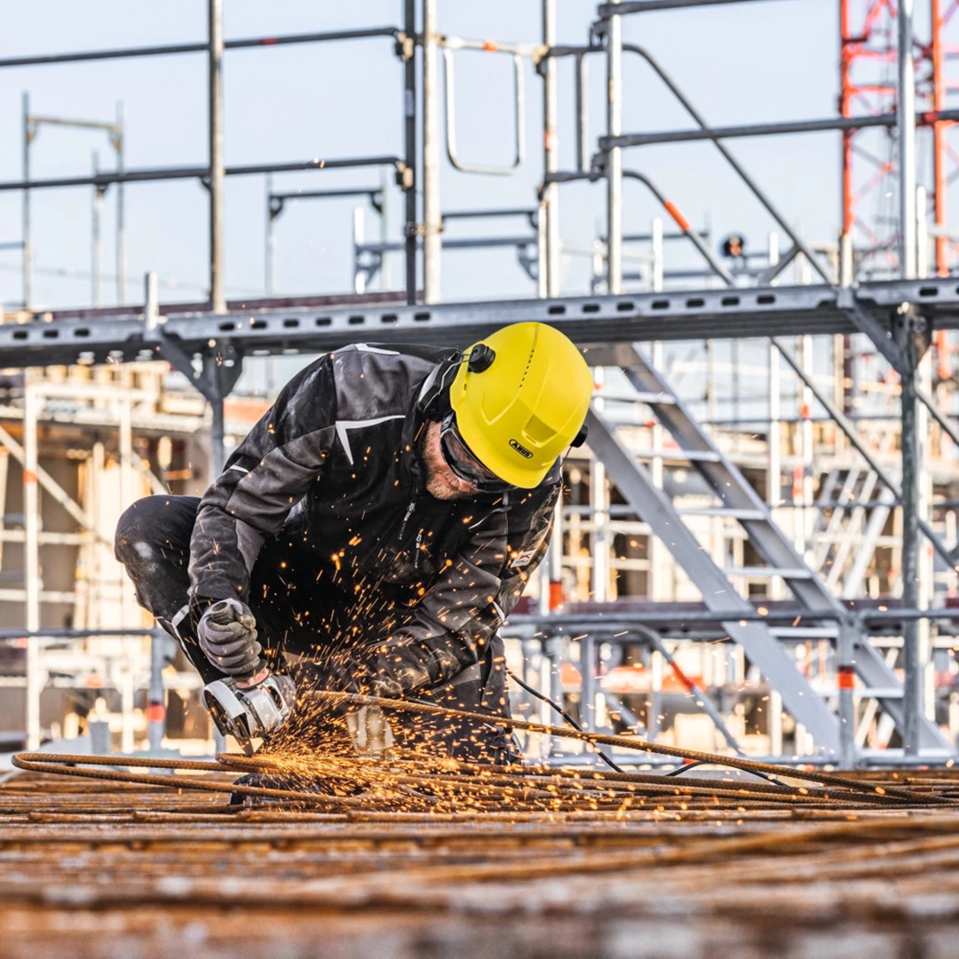 Mann mit gelbem Industrieschutzhelm Scator und Gehörschutz arbeitet auf einer Baustelle © ABUS