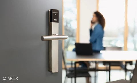 In the foreground, a modern office door with TECTIQ hardware. A woman on the phone in the background.